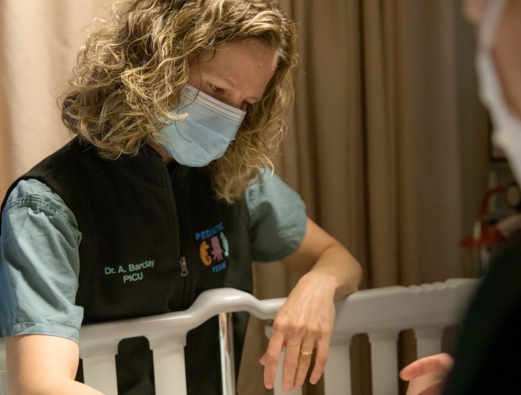 Physician leaning over crib providing care to infant 